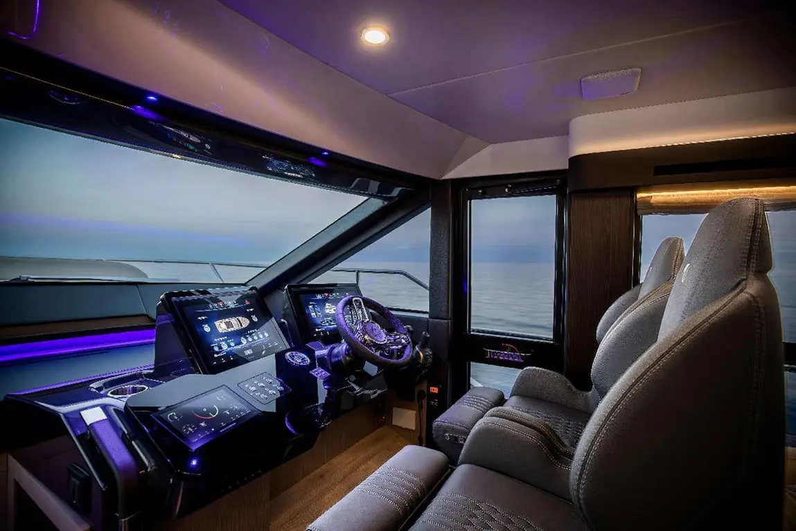 Modern boat cockpit with two ergonomic seats, high-tech displays showing navigation, and a panoramic view of the sea.